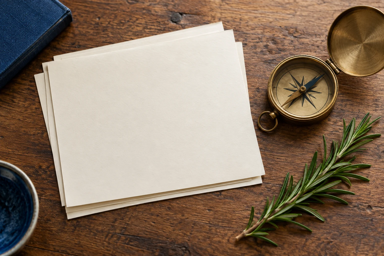 An artistic still life of presentation notes, a brass compass and rosemary on a timber table