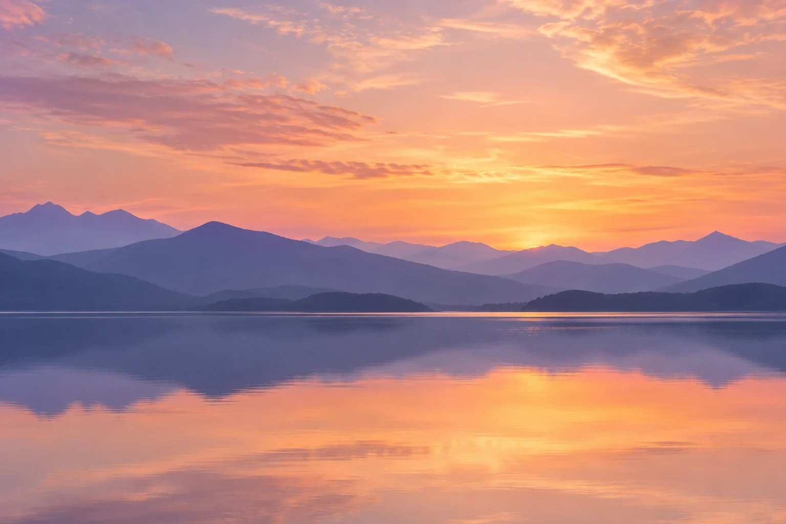 An artistic view of lavender-blue mountains reflected in a still lake at sunset